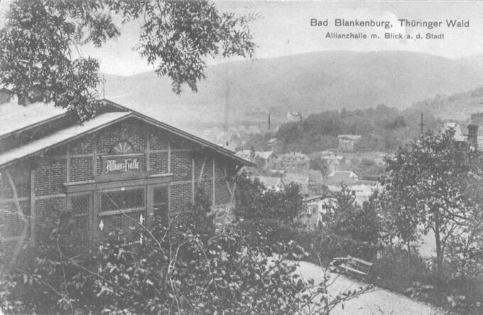 Historische Ansichtskarte von Bad Blankenburg im Thüringer Wald. Im Vordergrund ist die Allianzhalle zu sehen, umgeben von Bäumen. Im Hintergrund erstreckt sich die Stadt mit sanften Hügeln und einem bewaldeten Landschaftsbild.